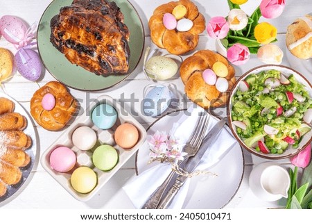 Festive served Easter dinner or brunch table, with Easter egg, tulip flower bouquet, traditional Easter foods - cake, cross buns, wreath bread, glazed ham and spring salad, white table background