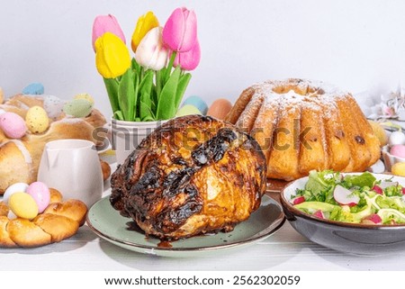 Festive served Easter dinner or brunch table, with Easter egg, tulip flower bouquet, traditional Easter foods - cake, cross buns, wreath bread, glazed ham and spring salad, white table background