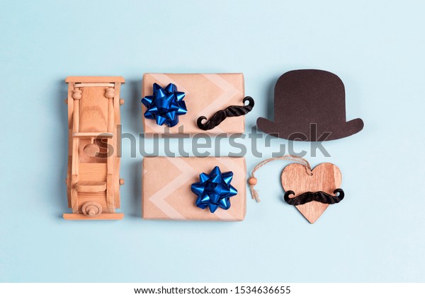 Festive set of gift boxes, mustache, paper hat\
and toy car on blue background. Flat lay, top view. International\
men\'s day concept.