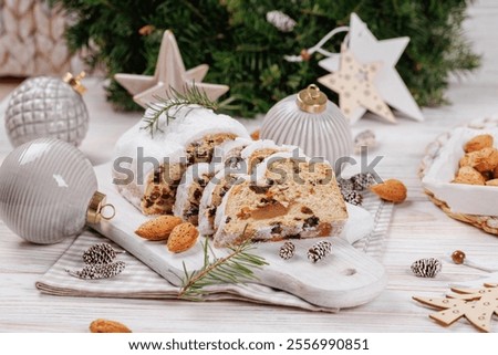 A festive setting featuring stollen bread slices, powdered sugar, almonds, and decorative ornaments creating a warm and inviting holiday scene.