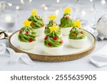 Festive stuffed eggs Christmas trees on a plate decorated with red and yellow peppers and parmesan. New Year