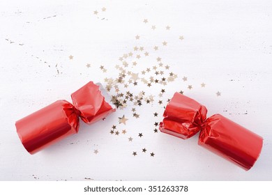 Festive surprise concept with opened red bon bon Christmas cracker and glitter stars on white wood table with copy space for your text here. 