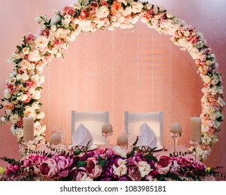 Festive table, arch, stands decorated with composition of violet, purple, pink flowers and greenery, candles in the banquet hall. Table newlyweds in the banquet area on wedding party.