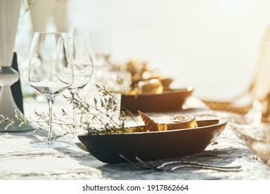 Festive table decor wine glasses and table setting in on the beach.. Preparing for an open-air party in the beach. Focus on dish with seashell.