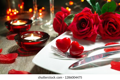 Festive table place setting for Valentines day dinner with red roses and burning candles