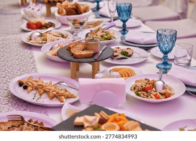 A festive table is set with an array of delicious dishes. Plates brim with vibrant salads, artisan breads, and tasty appetizers. Blue glasses catch the light, enhancing the inviting atmosphere.