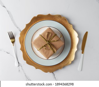 Festive Table Set With Gold Tableware And Gift Box At White Marble Table. Top View, Flat Lay, Concept Of Holiday Table Set