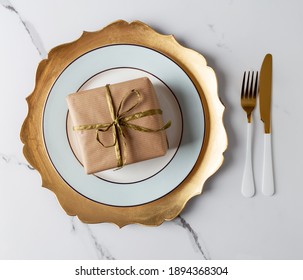 Festive Table Set With Gold Tableware And Gift Box At White Marble Table. Top View, Flat Lay, Concept Of Holiday Table Set