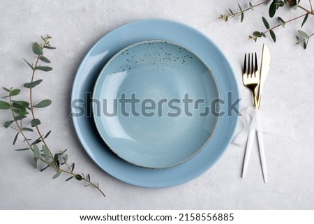 Festive table setting with blue ceramic plate, golden cutlery set and fresh eucalyptus leaves on grey concrete table top view. Plate mockup. Copy space, element for design