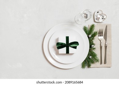 Festive table setting for Christmas dinner on a gray table. A gift in a plate, silver decorations on a gray background. View from above. Space for text.