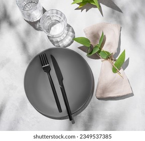 Festive table setting with dark grey plate and glasses for a celebration with eucalyptus branches on a light background with shadows. Restaurant menu concept. Top view - Powered by Shutterstock