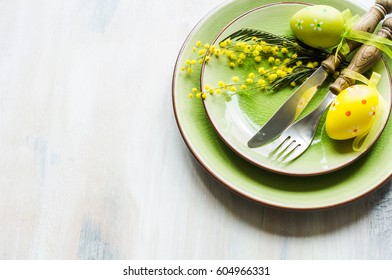 Festive Table Setting For Easter Dinner With Bright Easter Eggs And Mimosa Flowers On Rustic Plate