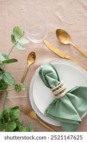 Festive Table setting for elegant dinner with white porcelain plates, glass, green napkin, gold cutlery and centre place. Copy space