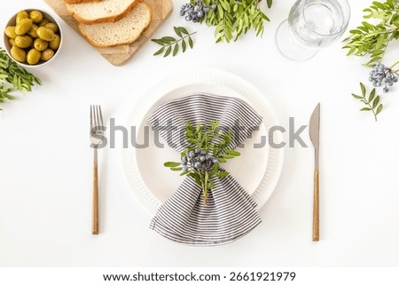 Festive table setting with empty plate, cutlery and napkin - green leaves decorated, bread and olives for dinner, flat lay. Top view.