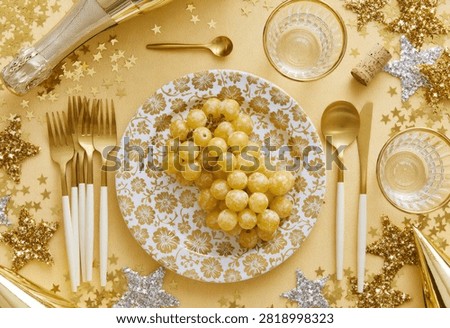 A festive table setting for New Year's Eve, featuring a plate of grapes, champagne, and sparkling decorations.