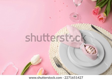 Festive table setting with painted egg, plates and tulips on pink background, space for text. Easter celebration