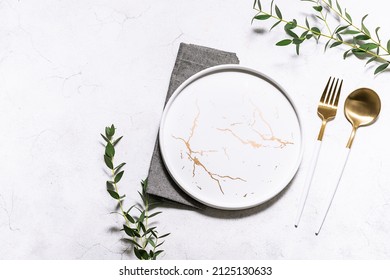 Festive table setting with white marble plate, golden cutlery set and fresh eucalyptus leaves on white rustic table top view. Copy space for your design. - Shutterstock ID 2125130633