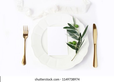 Festive Table Summer Setting With Golden Cutlery, Olive Branch, Porcelain Plate And  Silk Ribbon. Blank Card Mockup. Mediterranean Wedding Or Restaurant Menu Concept. Flat Lay, Top View.