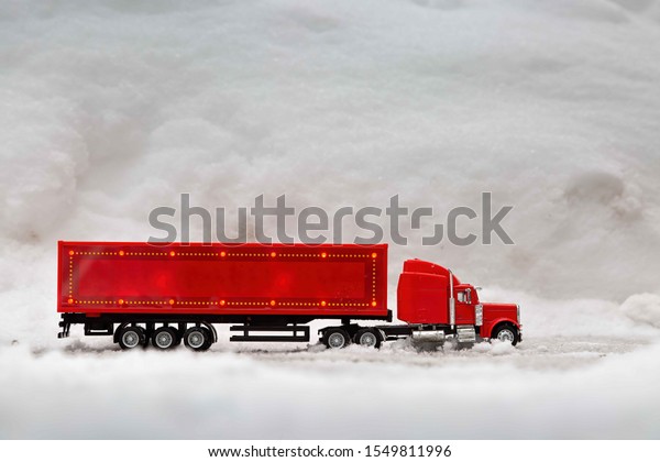 Festive truck in red. toy car\
rides on the background of real snowdrifts. Winter. Christmas\
holidays.
