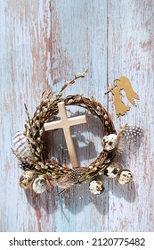 Festive willow wreath with eggs, cross and decorative angel on rustic wooden background. Easter, Palm Sunday holiday. prayer, faith, spiritual life, orthodox Church, religion concept. flat lay