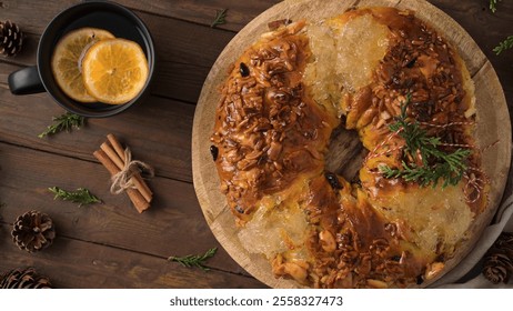 Festive wreath bread with nuts and honey glaze on a wooden board, accompanied by a cup of hot beverage with orange slices, cinnamon sticks, and pinecones - Powered by Shutterstock