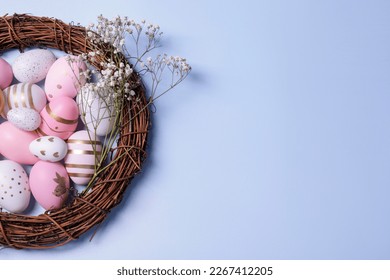 Festively decorated Easter eggs, vine wreath and gypsophila flowers on light blue background, top view. Space for text - Shutterstock ID 2267412205