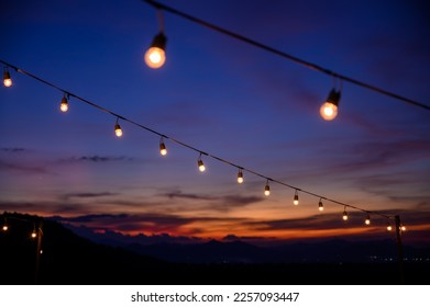 Festoon string lights decoration at the party event festival against sunset sky. light bulbs on string wire with copy space. Outdoor holiday background - Powered by Shutterstock