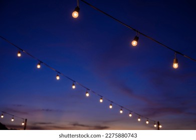 Festoon string lights decoration at the party event festival against sunset sky. light bulbs on string wire with copy space. Outdoor holiday background - Powered by Shutterstock