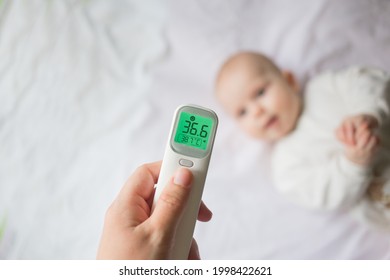 Fever and colds in an infant runny nose, flu or covid.Mom's hand holds a thermometer at the child's forehead and measures his temperature