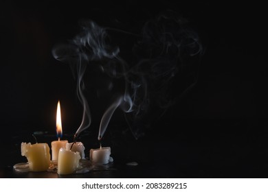 A few Candles isolated over dark background. Used, almost extinguished. Burned out. Copy space. Mystical smoke swirls in the darkness.