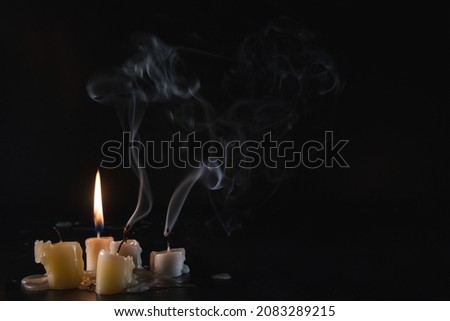 A few Candles isolated over dark background. Used, almost extinguished. Burned out. Copy space. Mystical smoke swirls in the darkness.