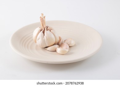 A Few Cloves Of Garlic On A Small White Plate Isolated In White Background