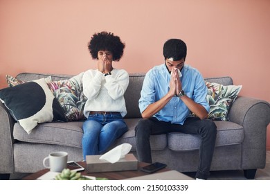 A Few Days Later He Got Sick Too. Shot Of A Young Couple Blowing Their Noses While Sitting On The Sofa At Home.