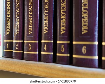 Few encyclopedia volumes, standing on a bookshelf, with close-up on golden volumes' numbers