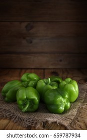A few fresh green peppers on burlap on a wooden table.  Fresh green peppers variety dolma. Low key, copy space.