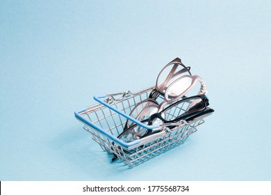 a few glasses in a toy metal shopping basket on a light blue background, glasses for adults and children, buying glasses in an optics store