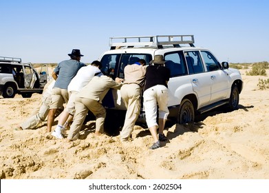 Few People Pushing A Car That Stuck In The Sand While Safari Desert