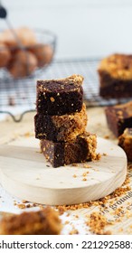 A Few Pieces Of Fudgy Brownies Topped With Biscuit Crumbs And Cookie Dough In The Middle Layer, Served In Stacks On A Wood Plate.