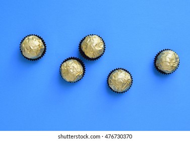 Few Round Shape Chocolates Wrapped In Golden Wrapper. Scattered Arrangement On Bright Blue Background.