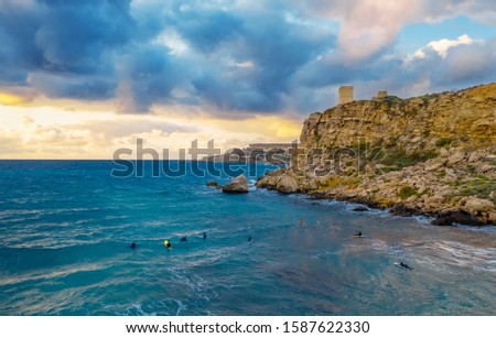 A few surfers in the sea on Ghajn Tuffieha bay. Aerial landscape, sunset, cloudy blue sky. Malta country