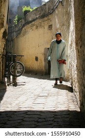 Fez, Morocco - March 1 2008 - A Woman In A Green Dress Walking Down A Narrow Alleyway In The Medina Of Fez, Morocco On A Sunny Day With Contrasting Shadows.  Image Has Copy Space.