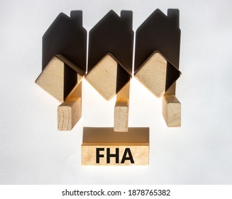 FHA symbol. Houses created by shadows from wooden cubes. The word 'FHA - federal housing administration' on a wooden block. Beautiful white background, copy space. Business and FHA concept.