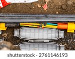 Fiber optic cable installation in underground trench, open splice closure with colorful microducts, telecommunications infrastructure construction, high-speed broadband internet deployment, FTTH techn