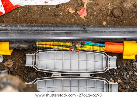 Fiber optic cable installation in underground trench, open splice closure with colorful microducts, telecommunications infrastructure construction, high-speed broadband internet deployment, FTTH techn