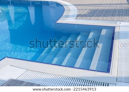 fiberglass plastic swimming pool entrance step with clean blue water at resort hotel spa area. Convenient access to the pool for children and the elderly.