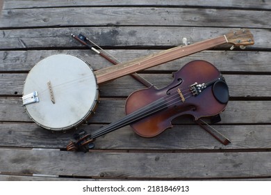 Fiddle and banjo on a wooden table with bow crossed behind. 