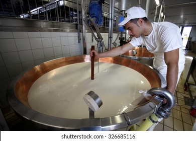 FIDENZA, ITALY - 11 SEPTEMBER 2014: A Worker Checks The Density Of Milk In Copper Vats During The Parmigiano-Reggiano Cheese Manufacturing Process At A Cheese Factory. 