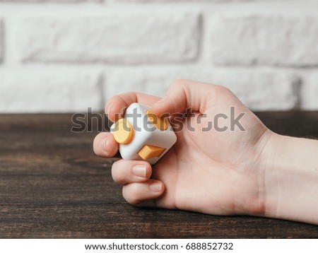 Fidget cube stress reliever in hand over brown wooden background. Fingers antistress toy in hand with copy space.