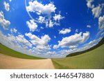 field dirt road, white fluffy clouds, green grass, fisheye photo with focus on the central part