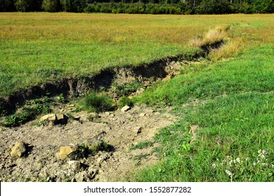 Field erosion on grass slope with erosive grooves made by water, soil erosion or destruction.